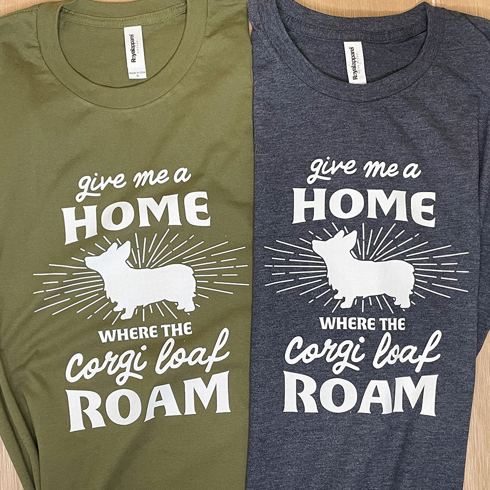 Two shirts which read  Give me a home where the corgi loaf roam lay folded side by side. One is Pine Green. One is a blended navy fabric.