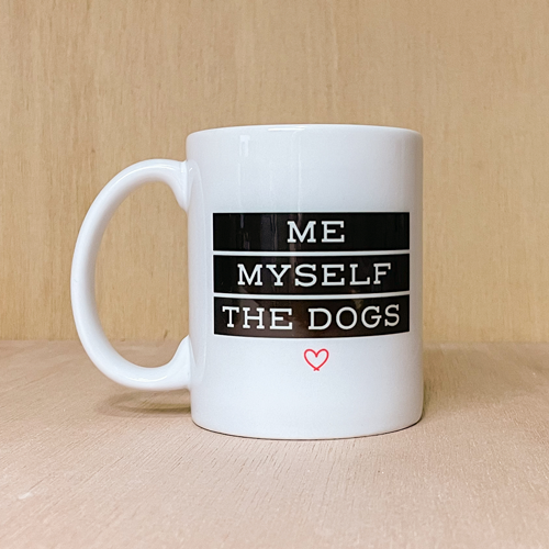 Me Myself and the Dogs coffee mug. Mug is white. Design is black with white text and red heart. Wood background.